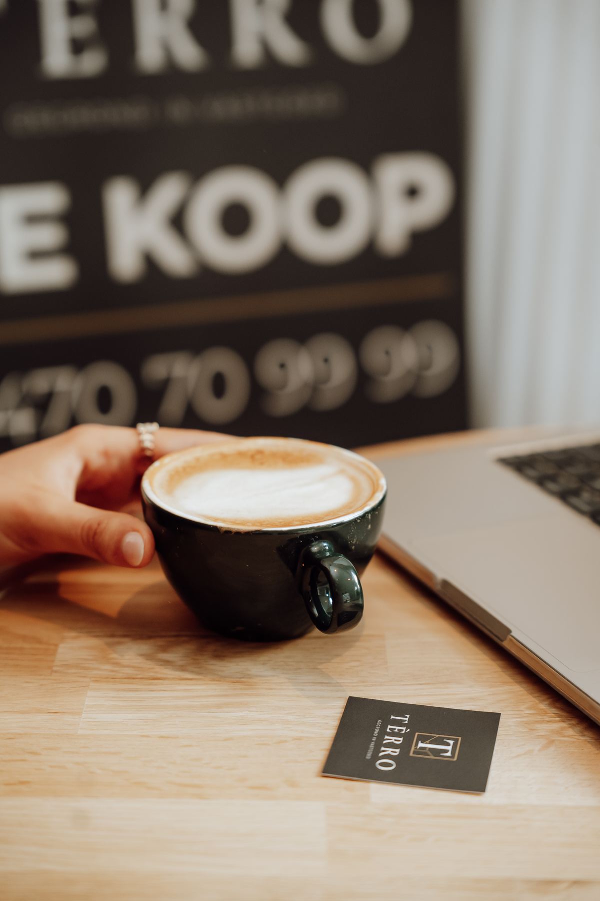Kop koffie naast een TÈRRO-bord Te koop en een visitekaartje